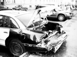 grayscale photo of wrecked car parked outside