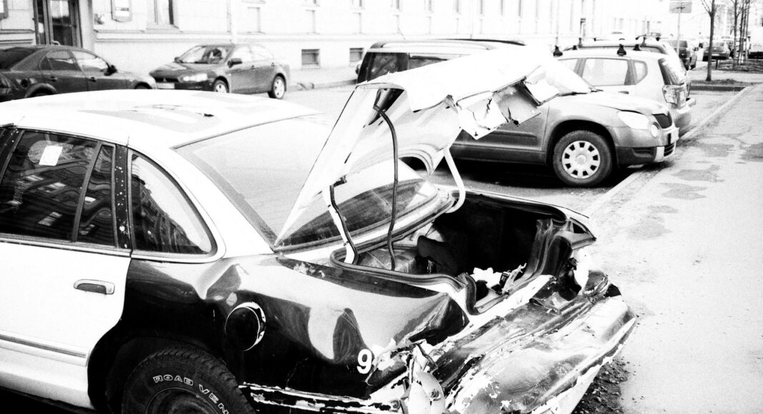 grayscale photo of wrecked car parked outside