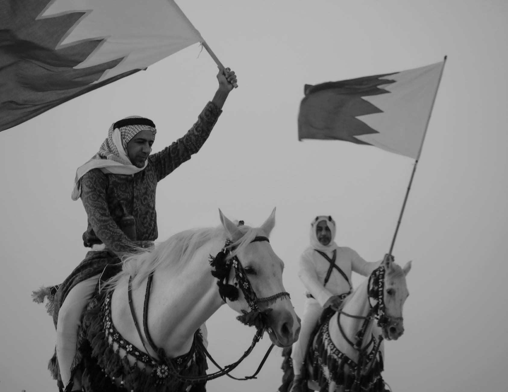 two men riding horses with bahraini flags in hands