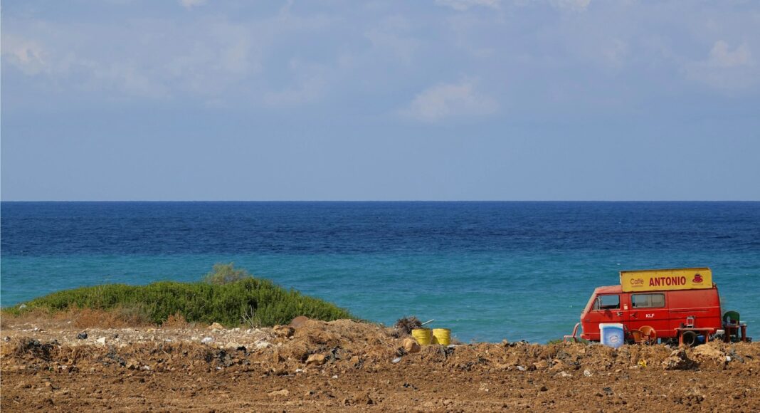 a red van parked on top of a dirt field next to the ocean