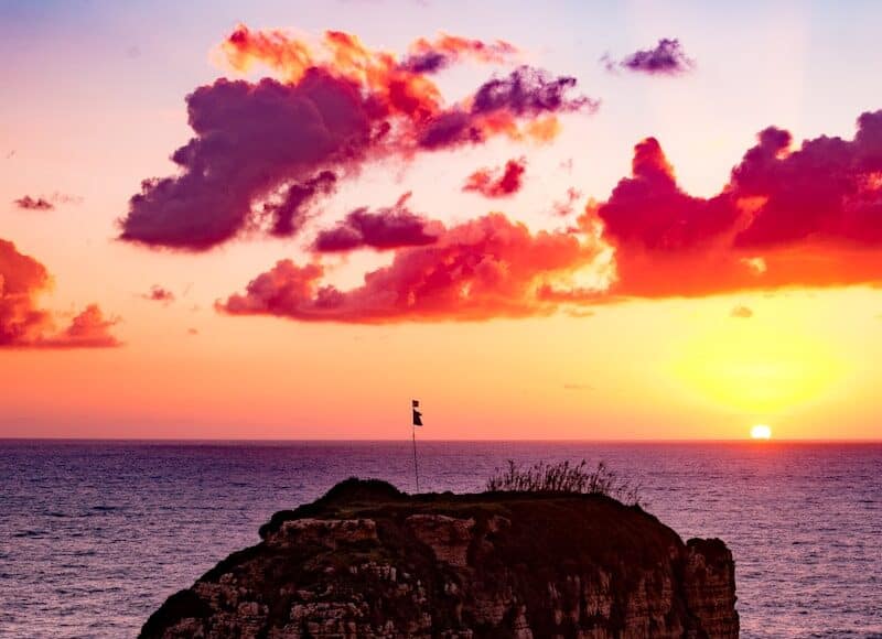 flag on top of rock formation in the middle of sea