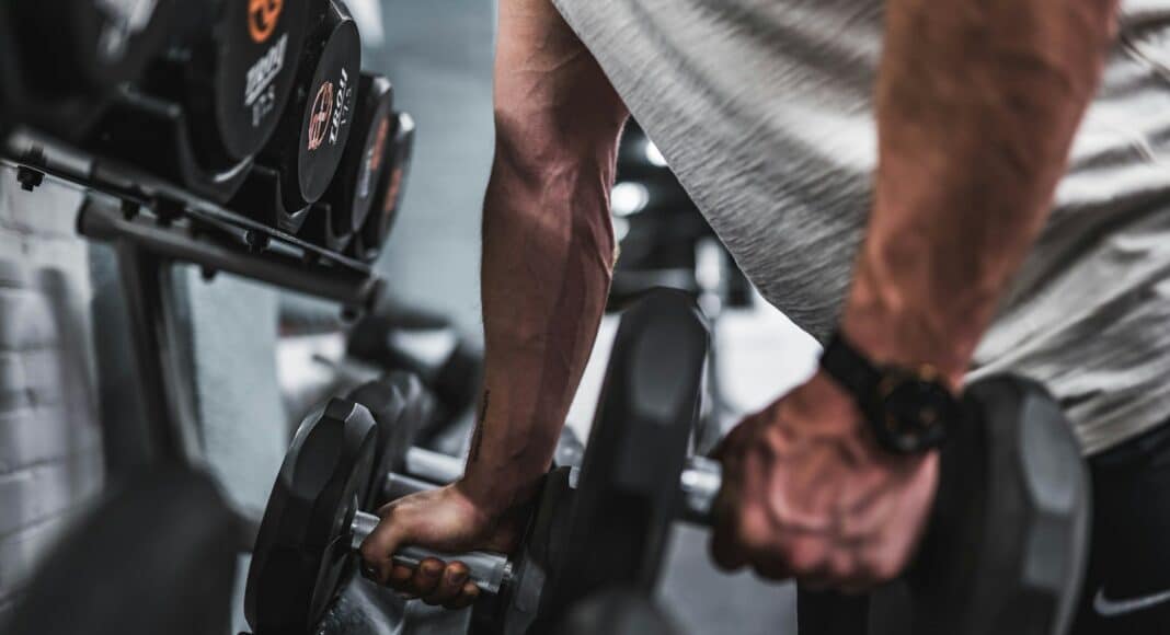 person in gray shirt holding black dumbbell