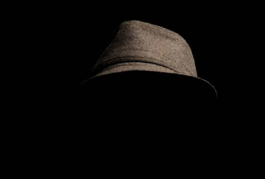 person wearing gray plaid notched lapel suit jacket and gray hat hiding face